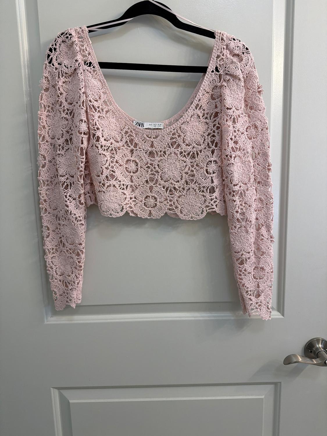 Light pink lace top with a floral design hanging on a black hanger over a white door.