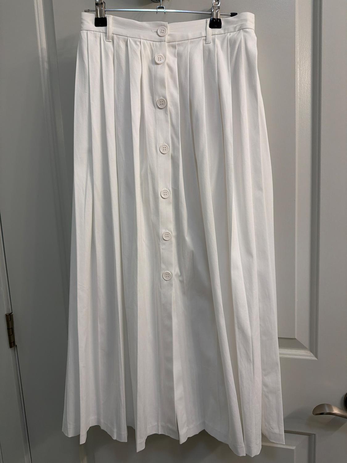 White pleated skirt with front buttons, hanging on a hanger over a gray door.