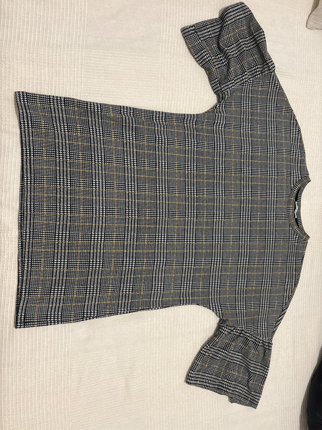 Short-sleeved blouse with a grey and black check print, on a beige background.