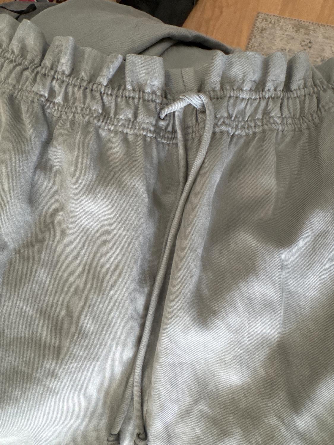 Grey trousers with an elasticated waist and adjustable drawstring, featuring soft fabric and visible texture against a light wood background.