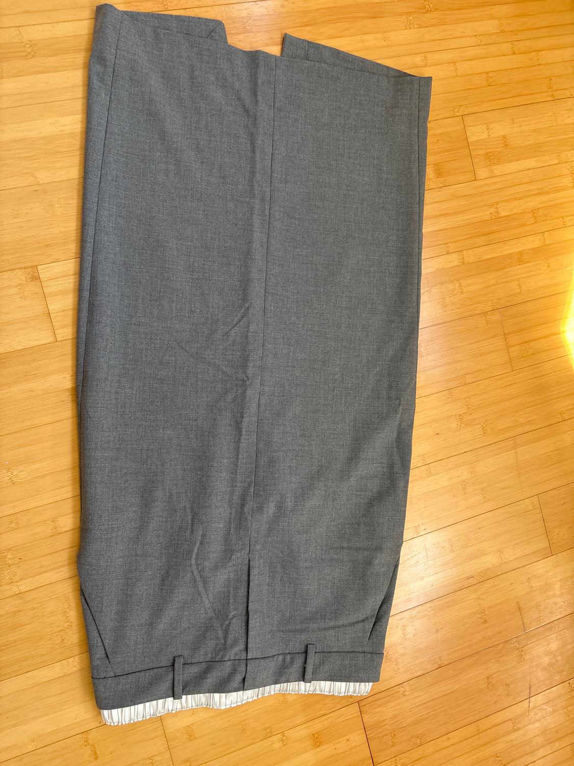 Gray fabric pants on a light wood floor, showing stitching details and a hem with a white lining.