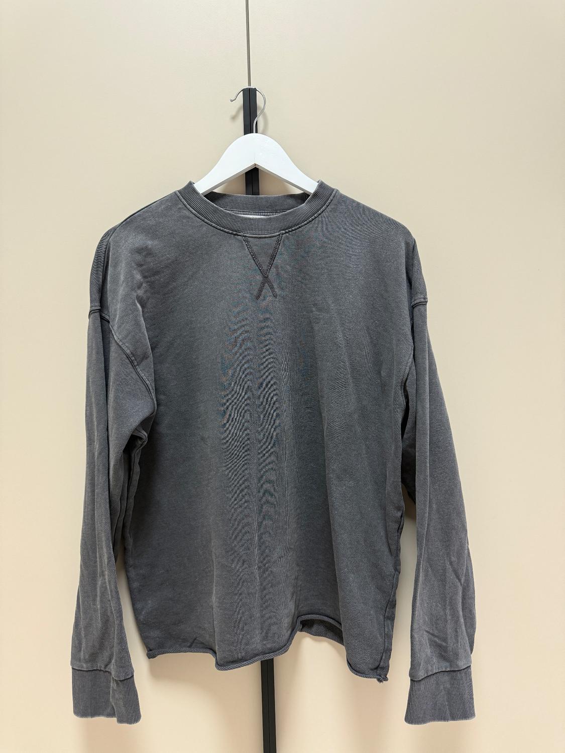 Grey long-sleeved sweatshirt hung on a white hanger against a beige background. Simple design with a round neck.