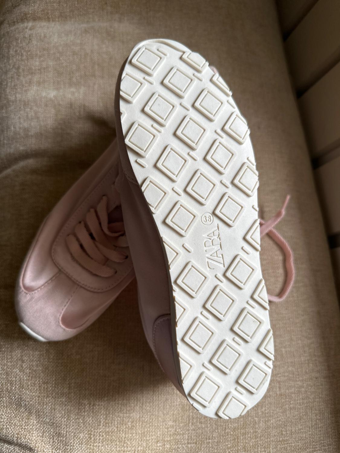 Pink trainers on beige fabric. One shows the white sole with a square pattern and the text ZARA (38). The other shows its laces.