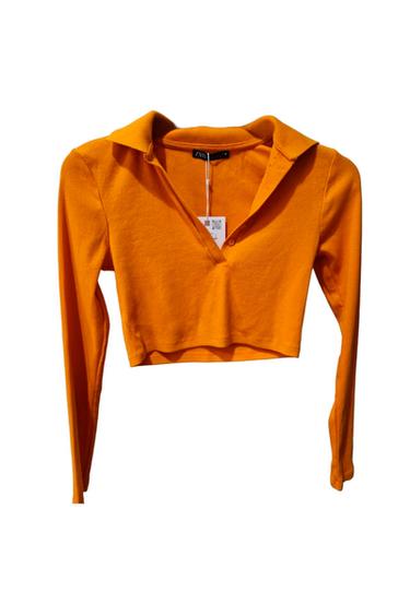 Orange long-sleeved cropped top with a polo collar, ribbed texture and V-neck with button on a white background. ZARA text on the label.