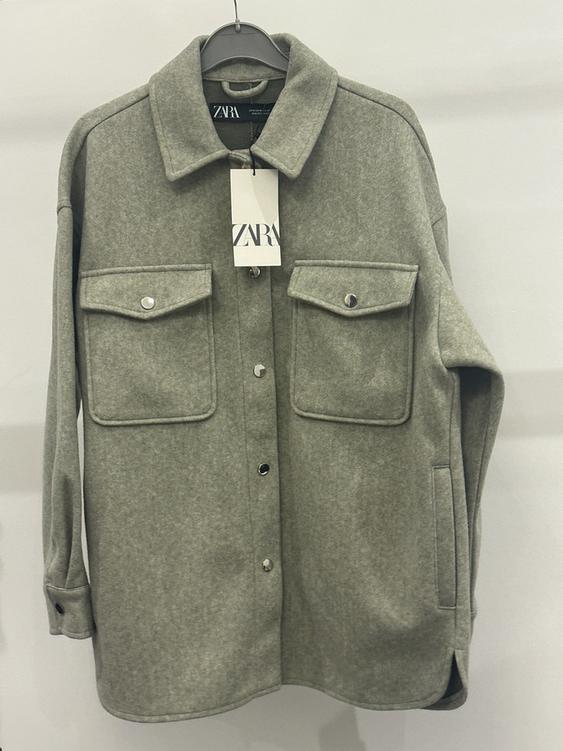 Grey wool shirt hanging on a hanger with ZARA tag, front flap pockets and metallic buttons.