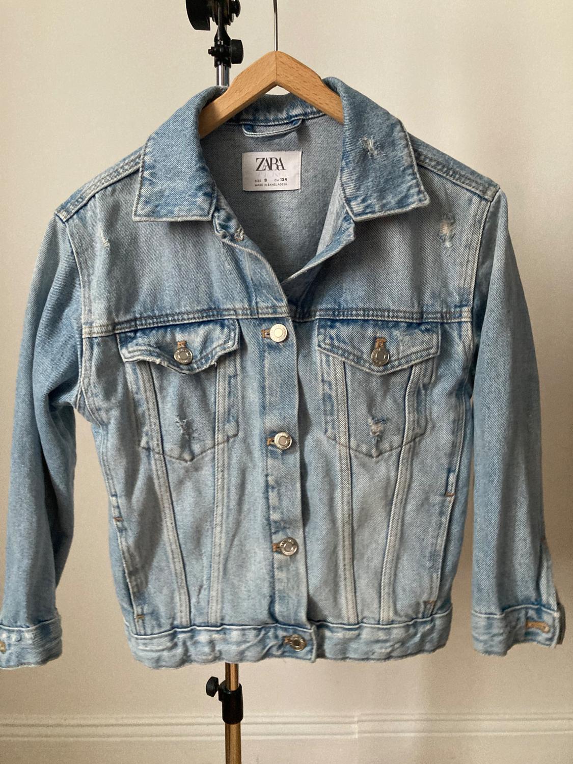 Front view of a light blue denim jacket with a classic collar, metal buttons and front flap pockets.