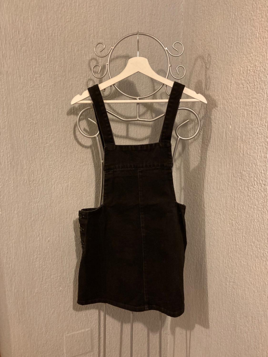 Front view of a black sleeveless dress with wide straps and side pockets.