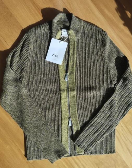 Ribbed knit jacket in shades of brown and green on a wooden floor. White label with "ZVA" text hanging from the collar.