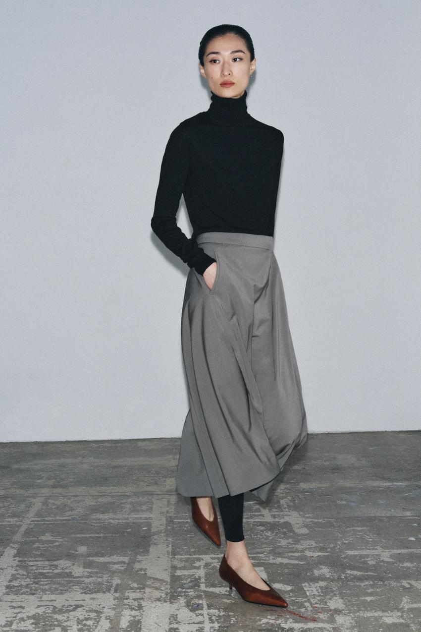 Gray midi skirt set with front pleat and side pockets, black turtleneck sweater, and brown shoes.