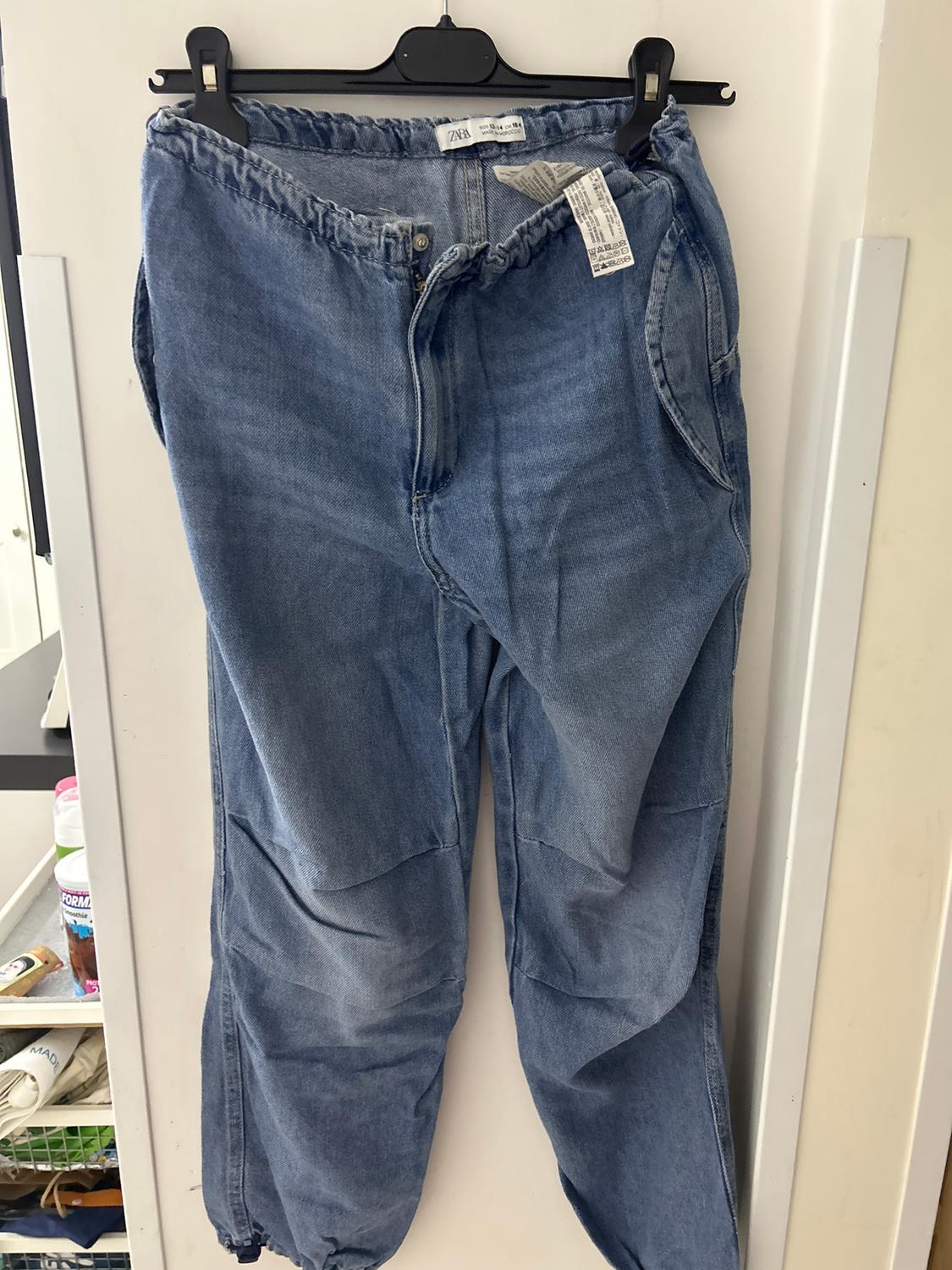 Light blue denim jeans hanging on a black hanger. Label visible on waistband. White background.