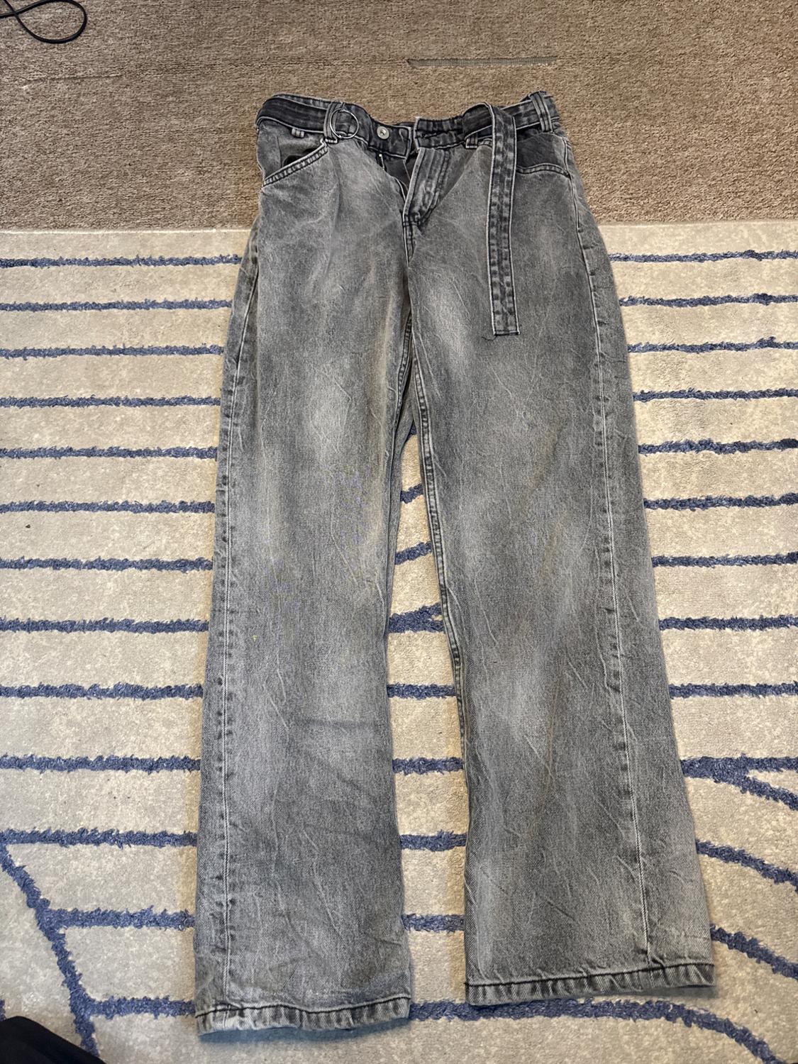 Worn grey denim jeans with a belt, on a blue striped rug. Relaxed composition in a casual style.