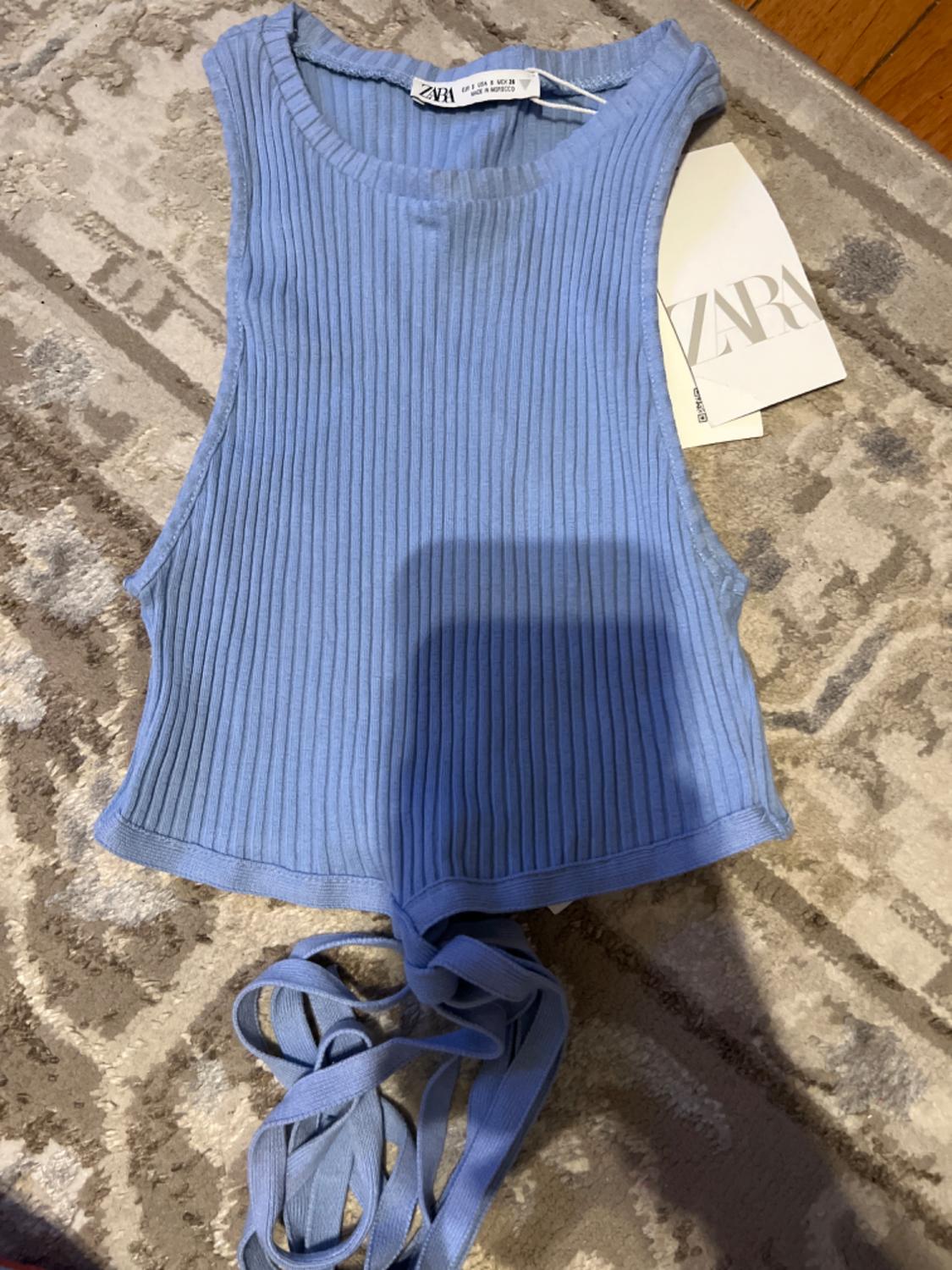 Sleeveless blue ribbed top with long tie at the bottom, visible Zara tag on beige rug with geometric design.