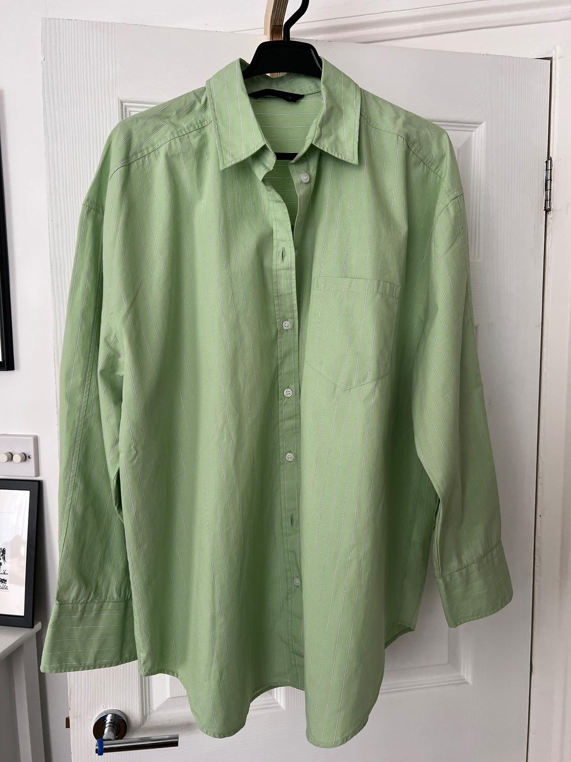 Light green shirt with thin vertical stripes, hanging on a black hanger over a white door.