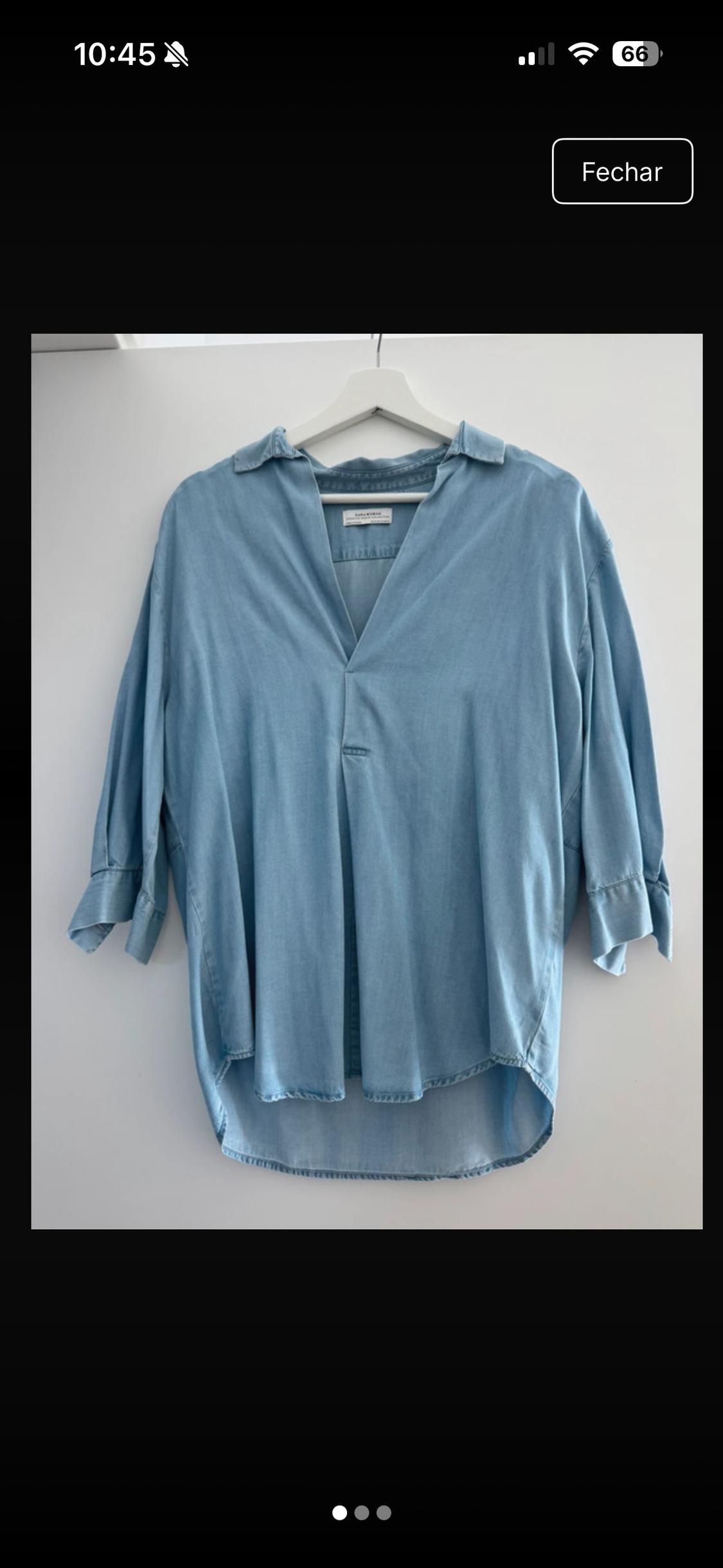 Loose-fitting light blue shirt with a V-neck and three-quarter-length sleeves, hanging on a white hanger against a white background. ZARA WOMAN label.