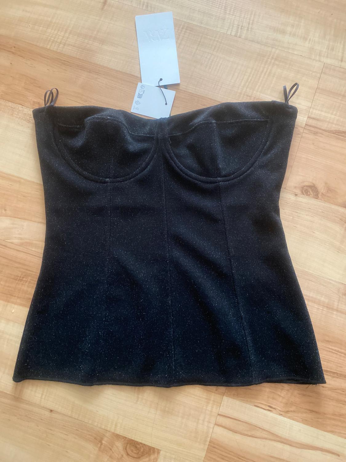 Black strapless top on light wooden floor. White tags hanging from the centre of the top.