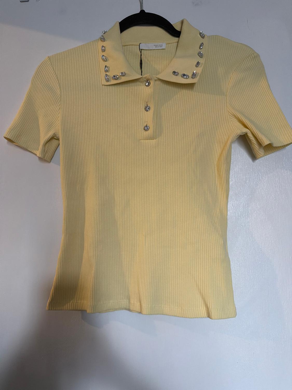 Yellow short-sleeved polo shirt with a collar decorated with sparkling stones, hanging on a black hanger against a white background.