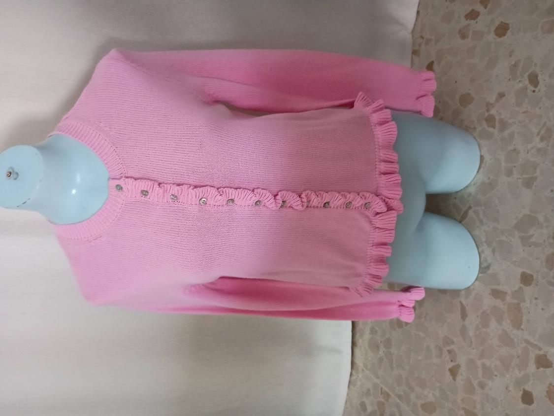 Blue mannequin with a pink knitted cardigan, front buttons and frill details on the edges, on a light background.