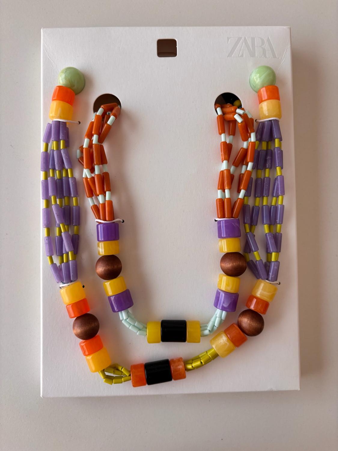 Beaded necklace in shades of orange, purple and yellow on white card with the text ZARA.