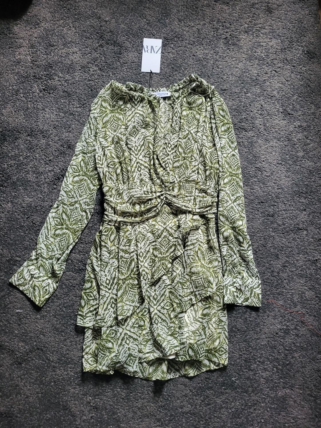 Short green dress with white geometric print on grey carpet. Label visible with "NM" logo.