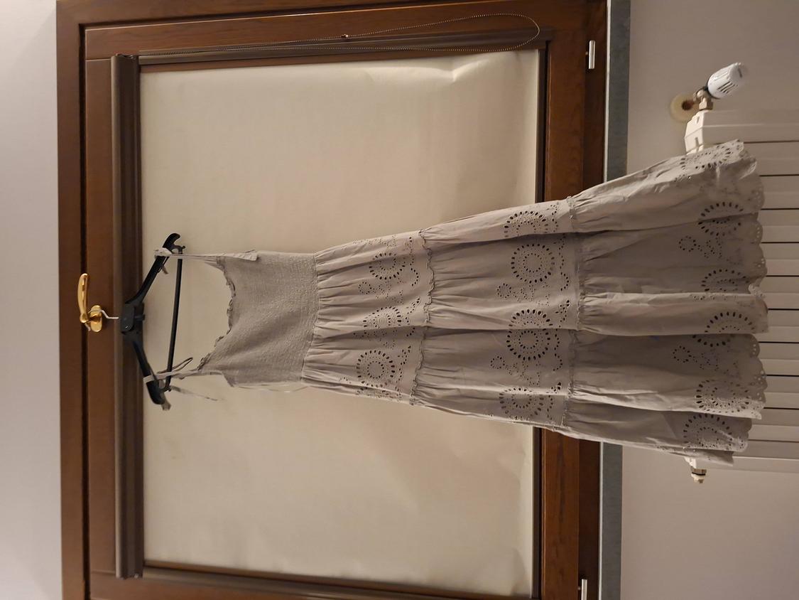 Light grey dress with circular embroidery hanging on a black hanger in front of a wooden window.
