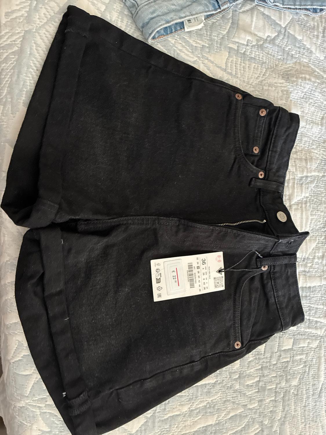 Black denim shorts with a hem, placed on a bedspread. Label with the text "36" and "€ 22.95".