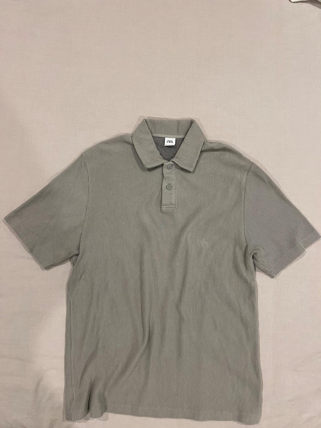 Grey short-sleeved polo shirt with a fine striped texture on a beige background. Visible label with "ZARA" text on the collar.