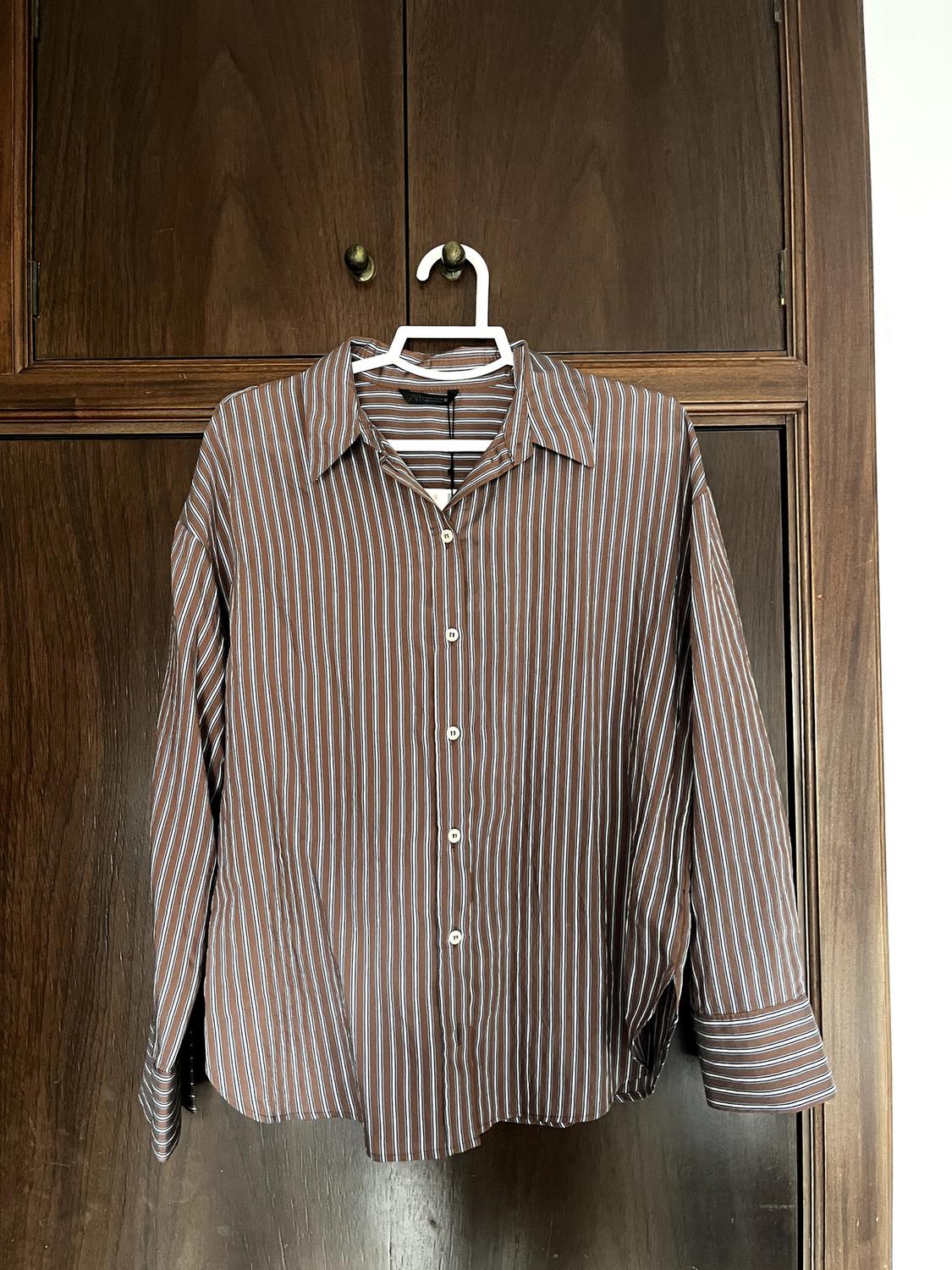 Brown and white striped shirt hanging on a white hanger in front of a dark wooden door.
