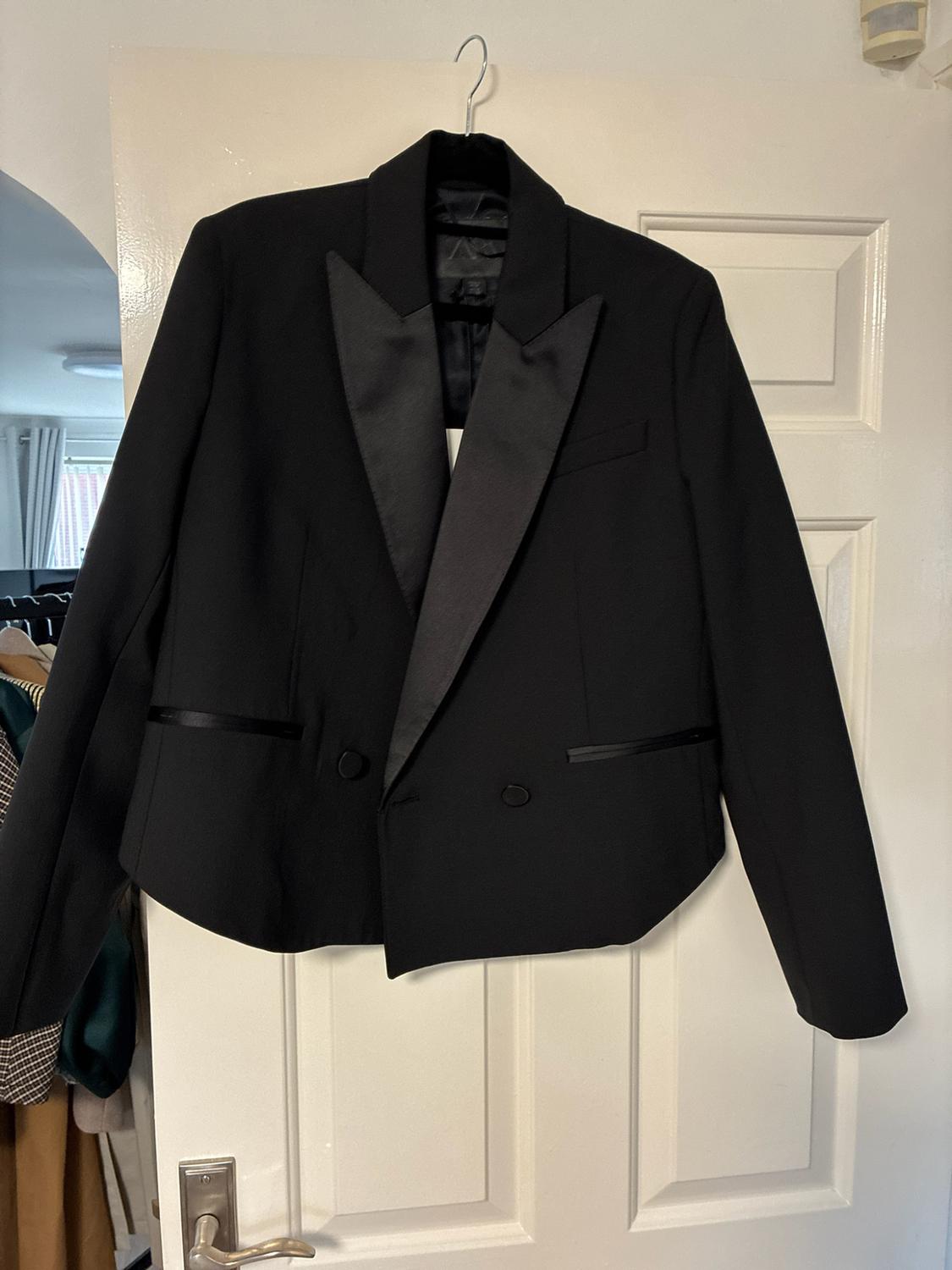 Black blazer with satin lapels hanging on a white door. In the background
on the left, a room with a coat rack can be seen.