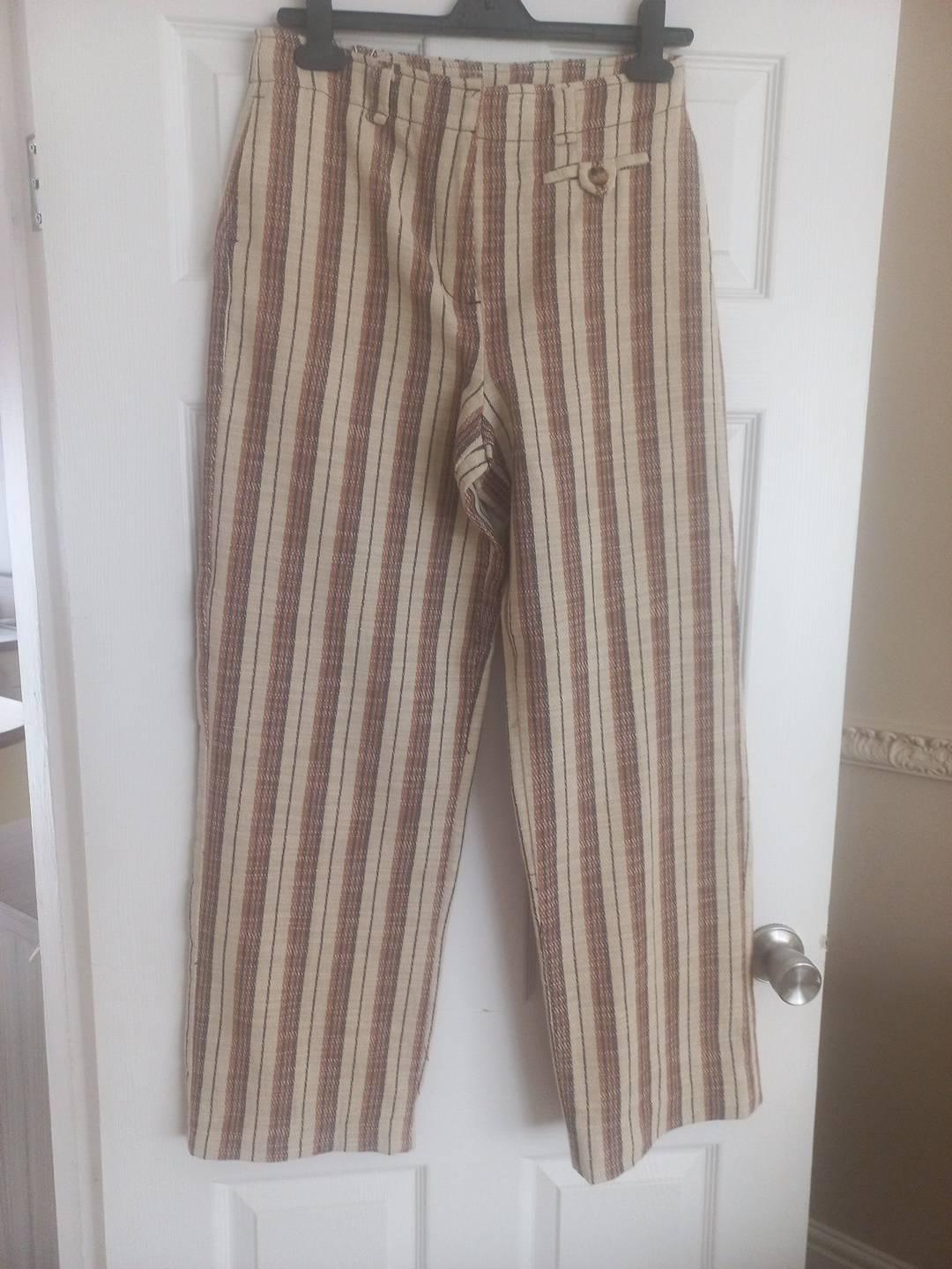 Beige and brown vertical striped trousers hanging on a black hanger over a white door with a metallic knob.