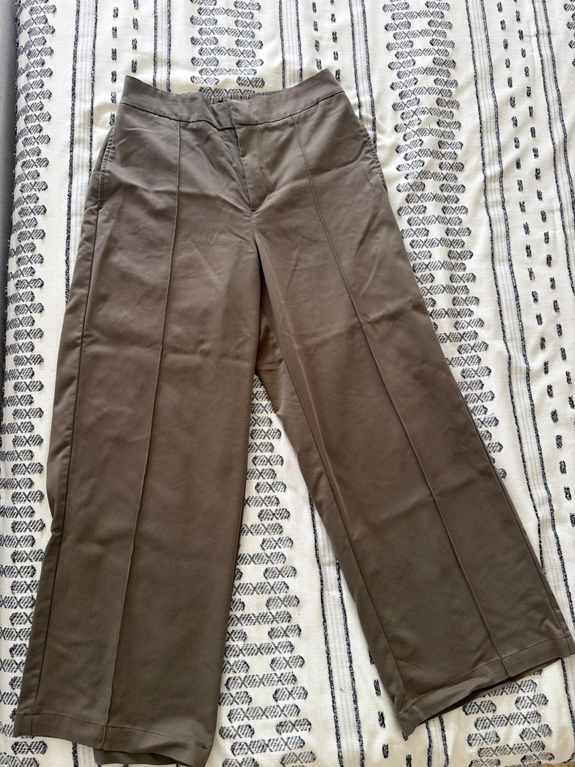 Brown wide-leg trousers with front seams, laid out on a white fabric with a black geometric print. Casual style.