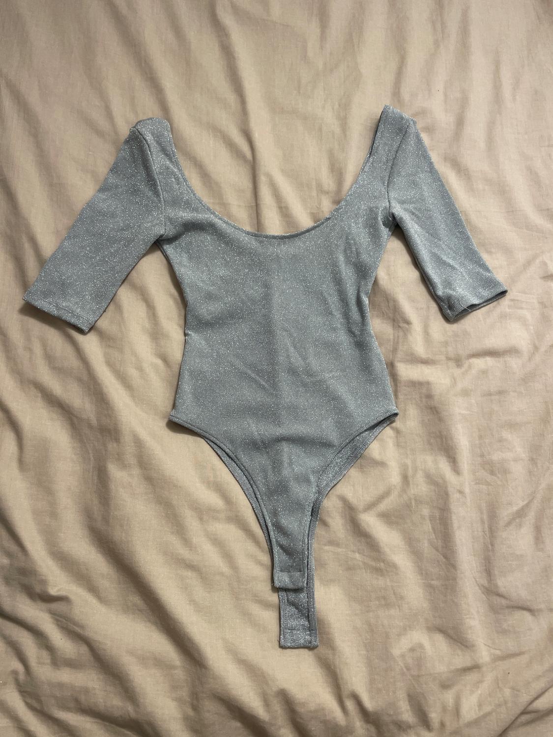 Shiny grey three-quarter sleeve, deep-cut bodysuit, over a crinkled beige fabric.