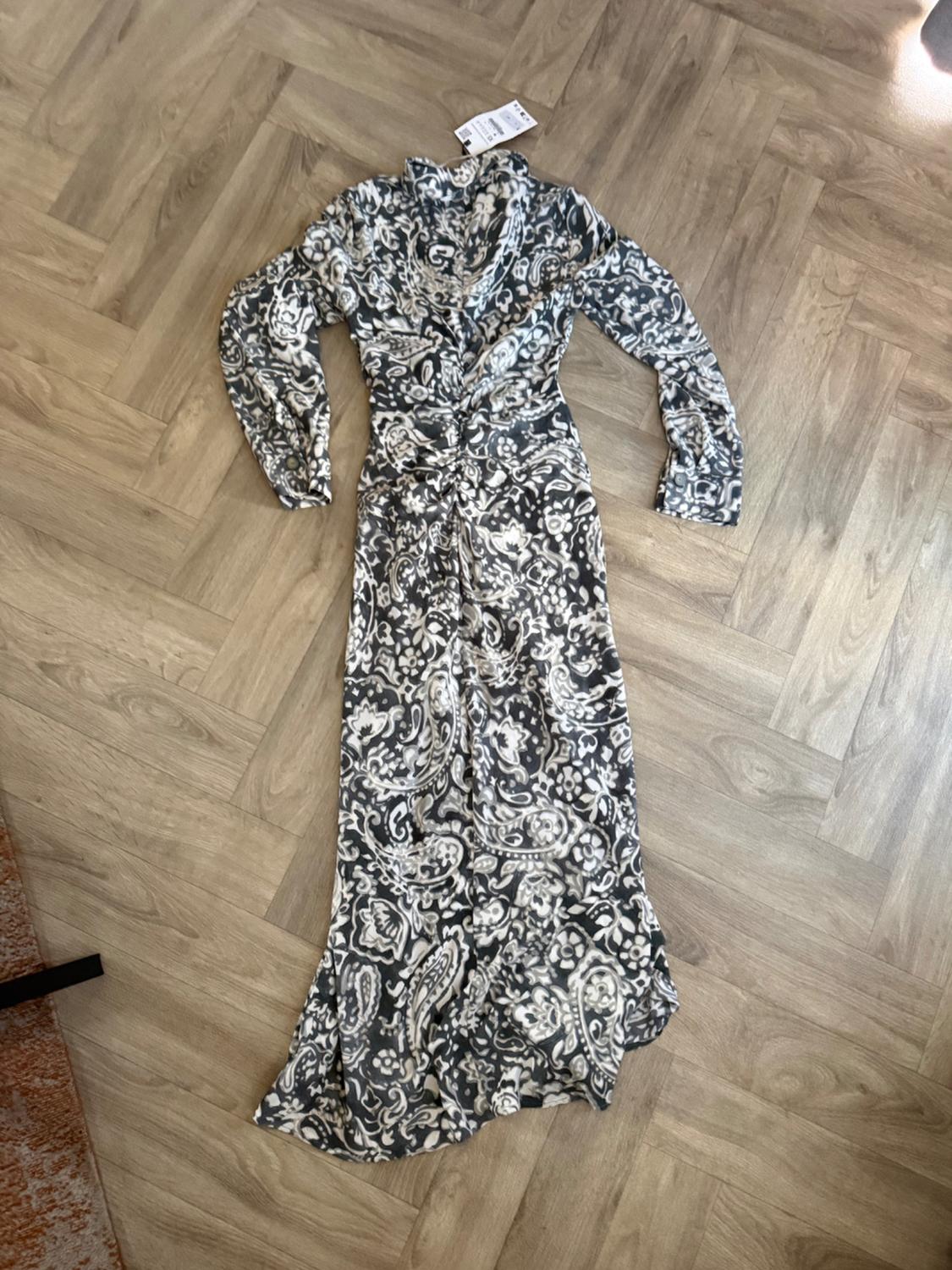 Long-sleeved V-neck maxi dress with a grey and white print and front ruching, on a wooden floor.