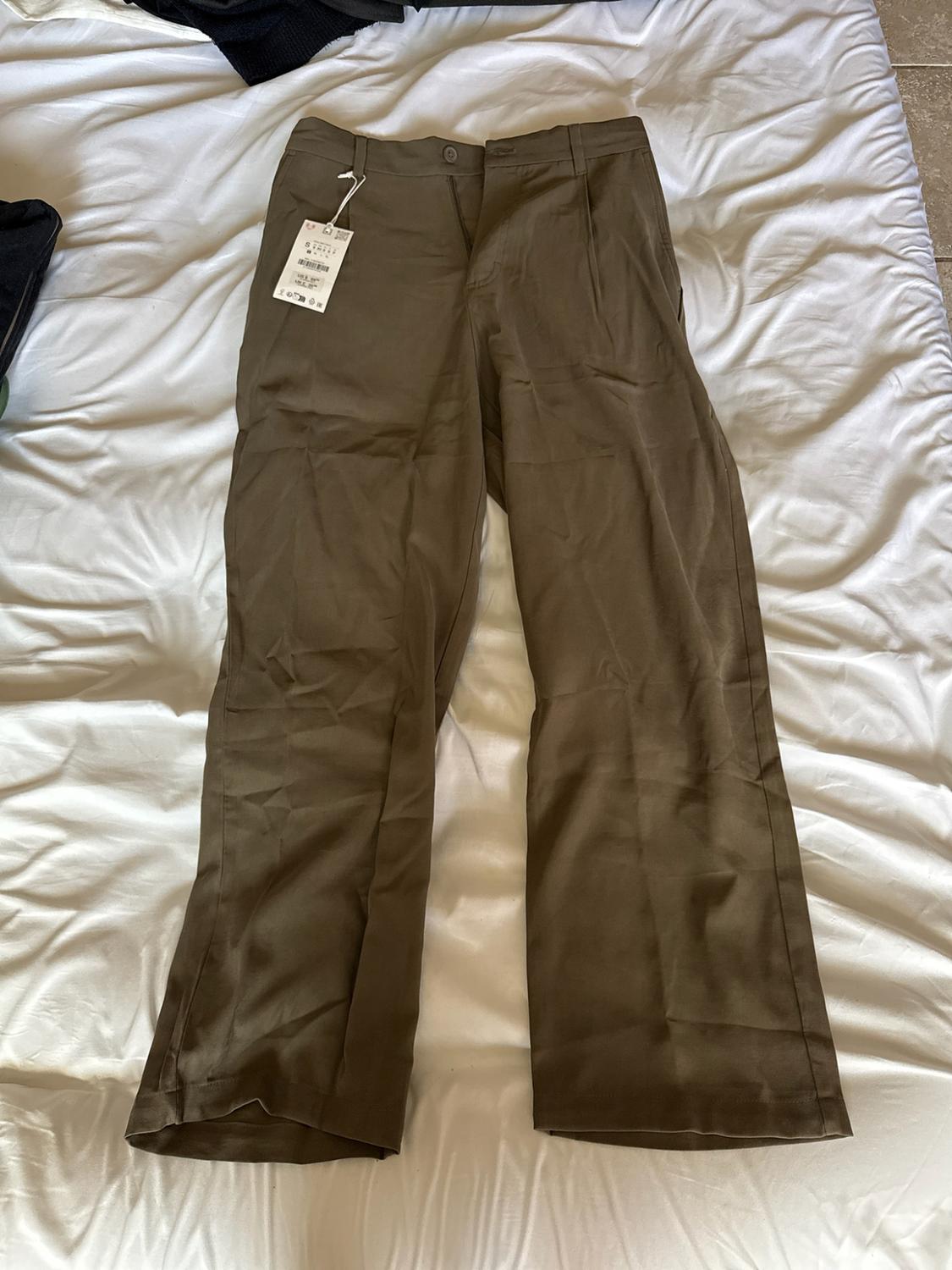 Brown straight-leg trousers with a label, laid out on crumpled white sheets.