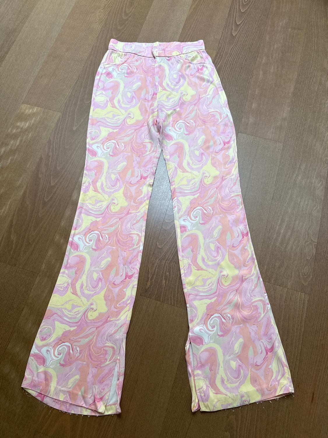 Flared trousers with swirl print in shades of pink, yellow and white, on brown wooden floor.