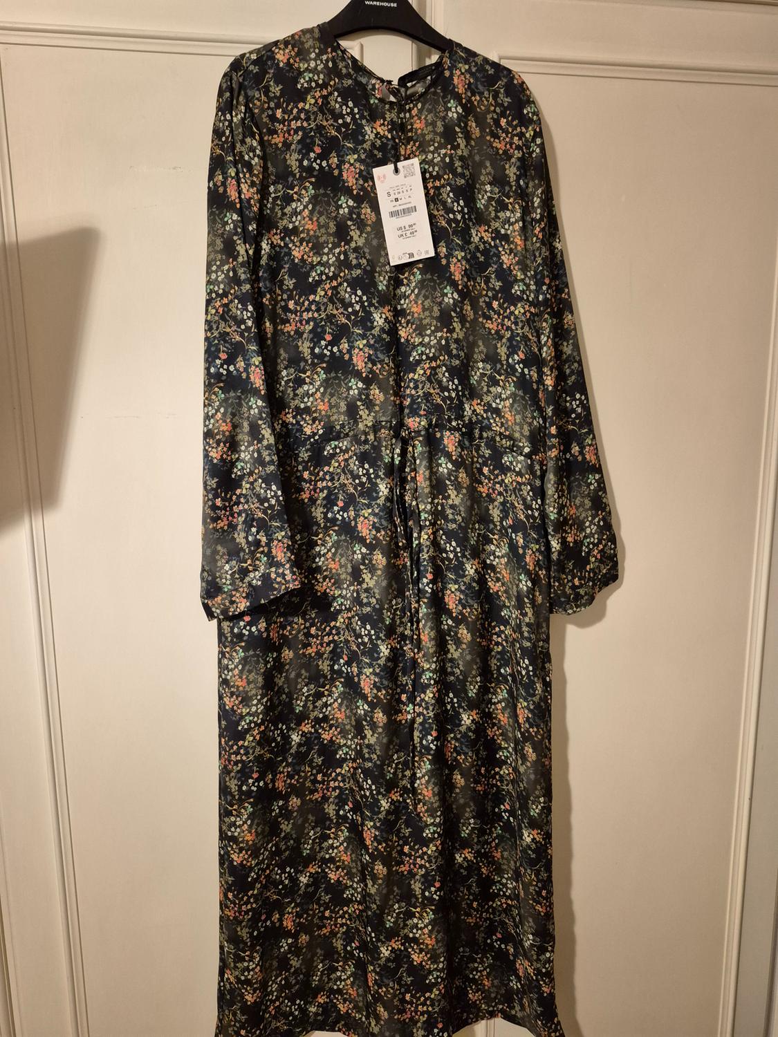 Long-sleeved maxi dress with a dark-toned floral print, hanging on a black hanger. Label visible on the chest.