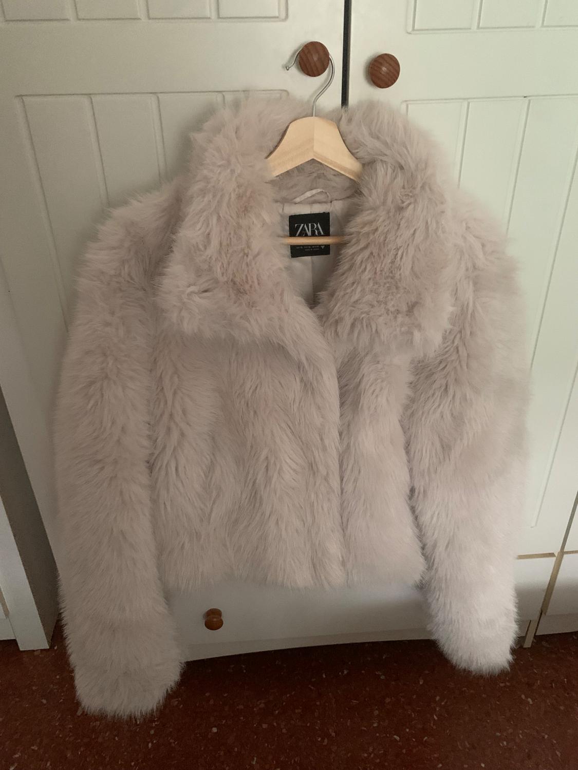 Cream faux fur jacket hanging on a wooden hanger in front of a white wardrobe. Visible label: ZARA.