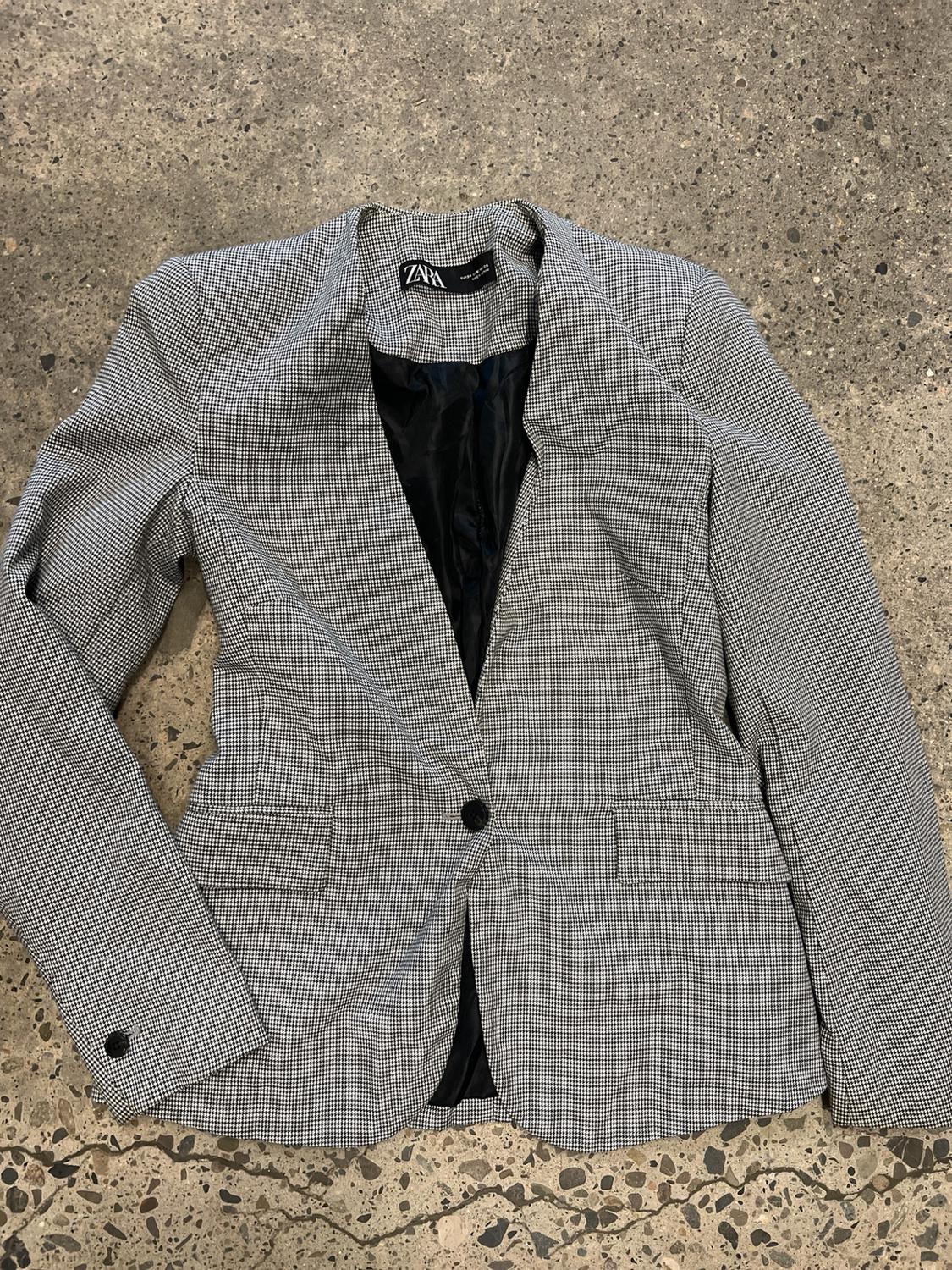 Black and white houndstooth blazer with one button, laid out on a stone floor. ZARA label visible on the inside.