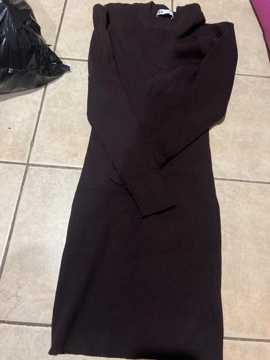 Black, long-sleeved, ribbed dress on a light tiled floor. Black bag visible in the top left corner.