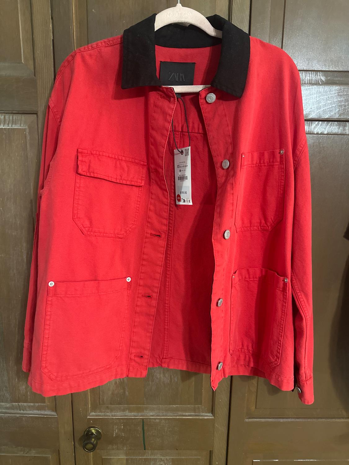 Red jacket with a black collar hanging on a hanger. Visible tag with a price of 59.90. Wooden door background.