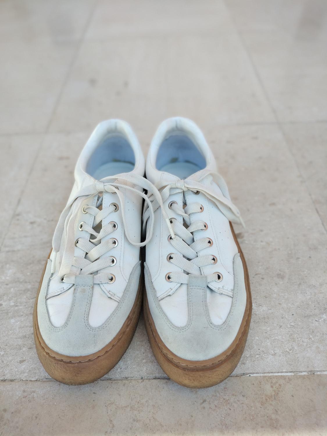 White casual-style trainers with grey suede details and a thick brown sole, photographed on a light-tiled floor.