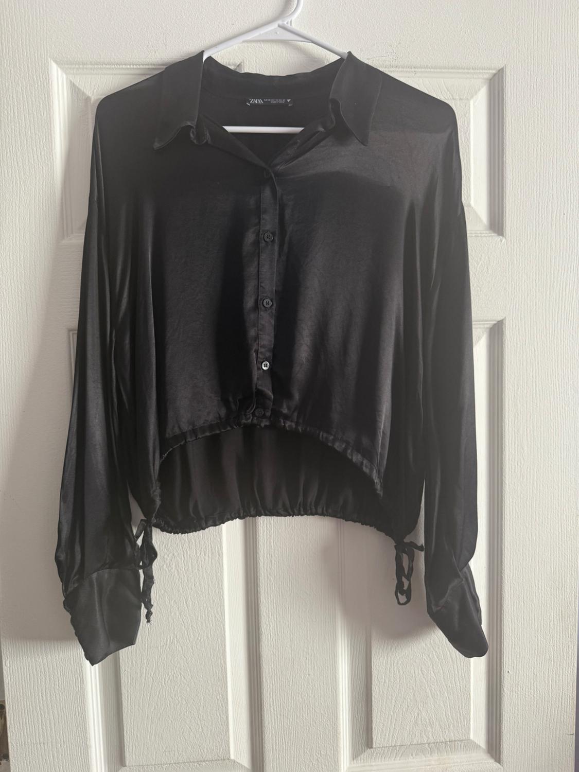 Long-sleeved satin black shirt hanging on a white hanger over a white door.