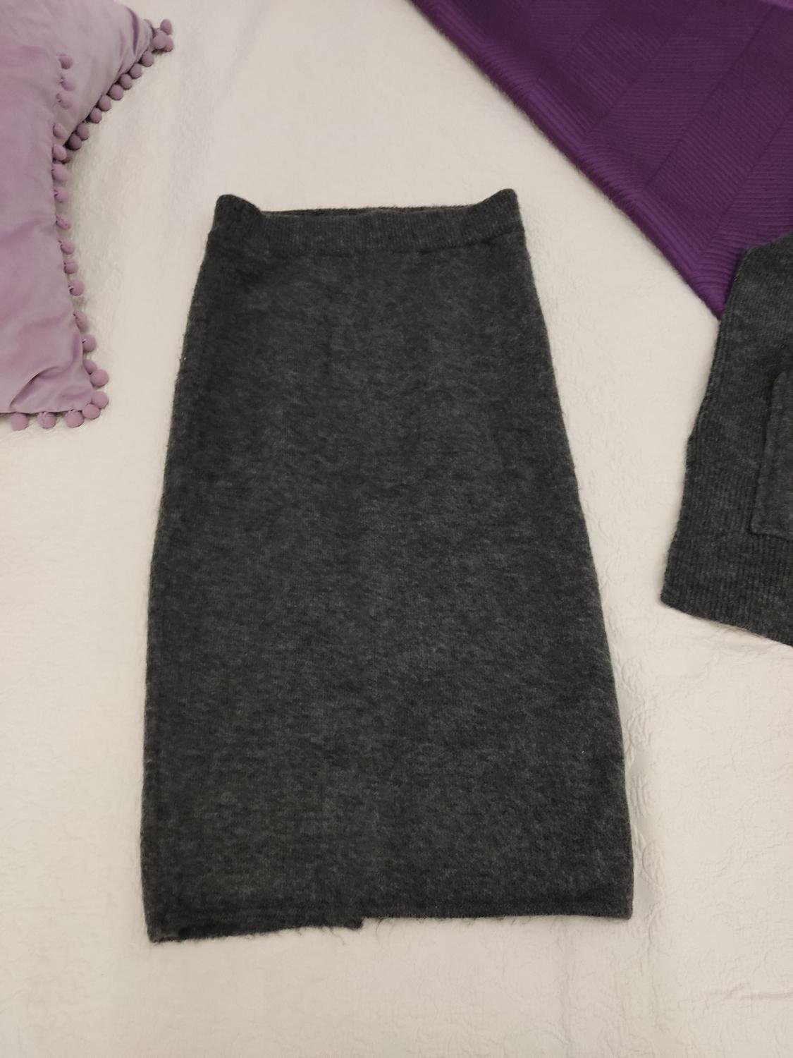 Grey wool skirt on a white bed, next to purple cushions. Cosy and relaxed atmosphere.