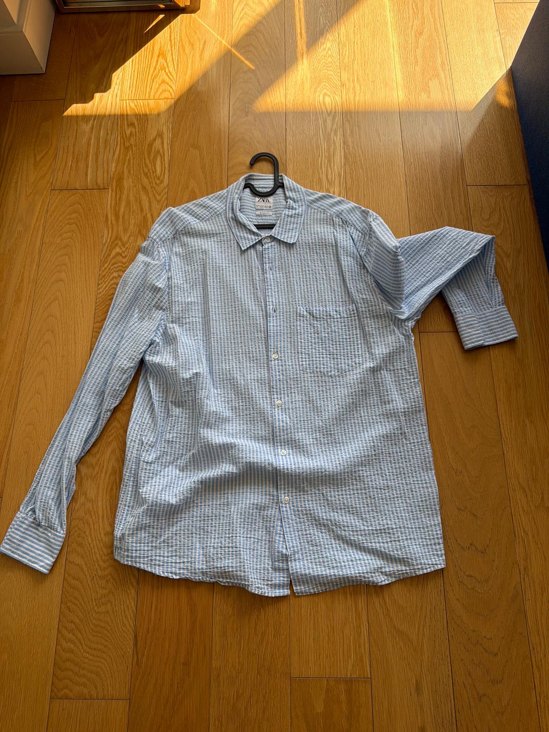 Blue and white plaid shirt on a wooden floor, hanging on a black hanger. Sunlight partially illuminates the scene.