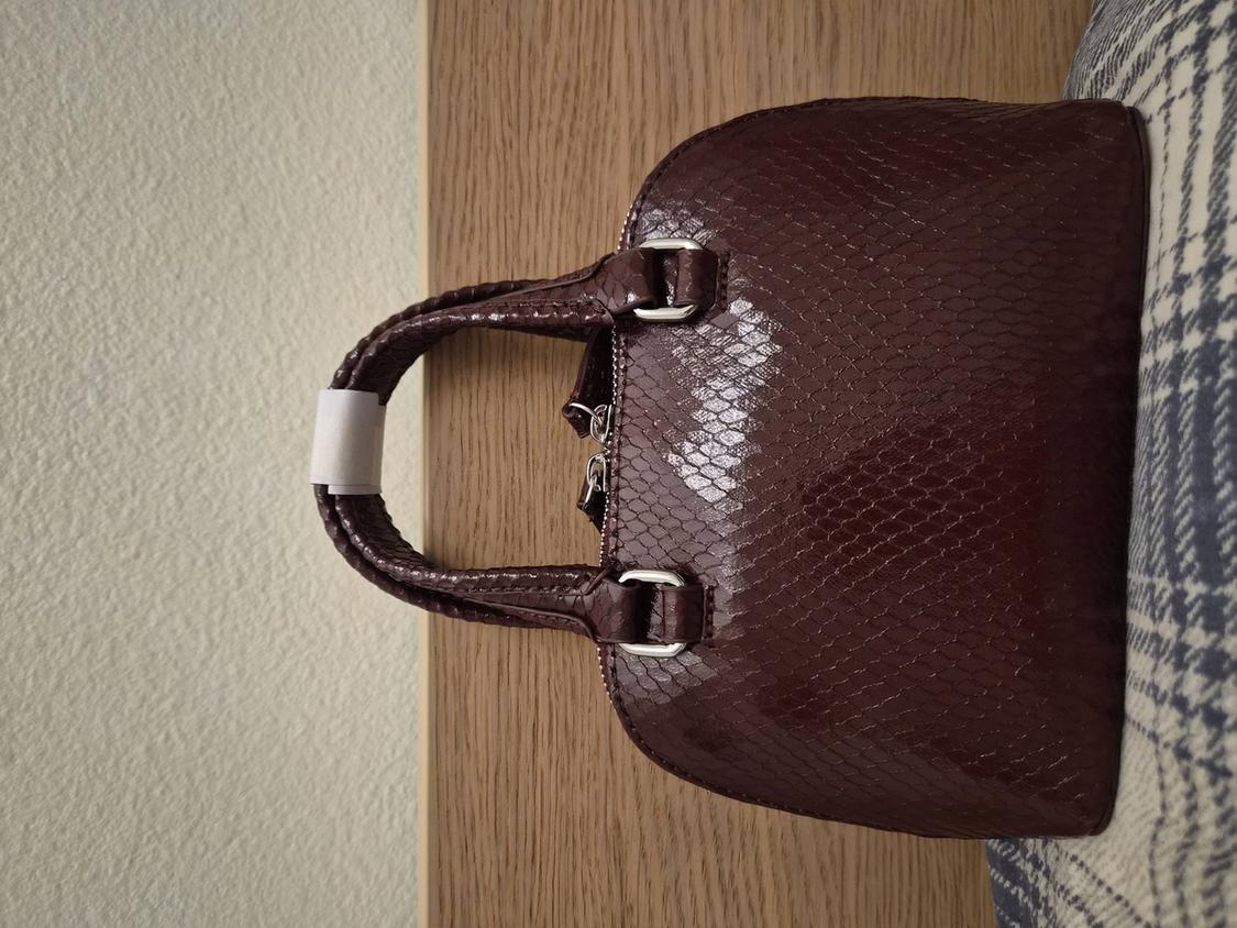 Brown snakeskin-textured bag with short handles and metallic details, resting on a wooden surface.