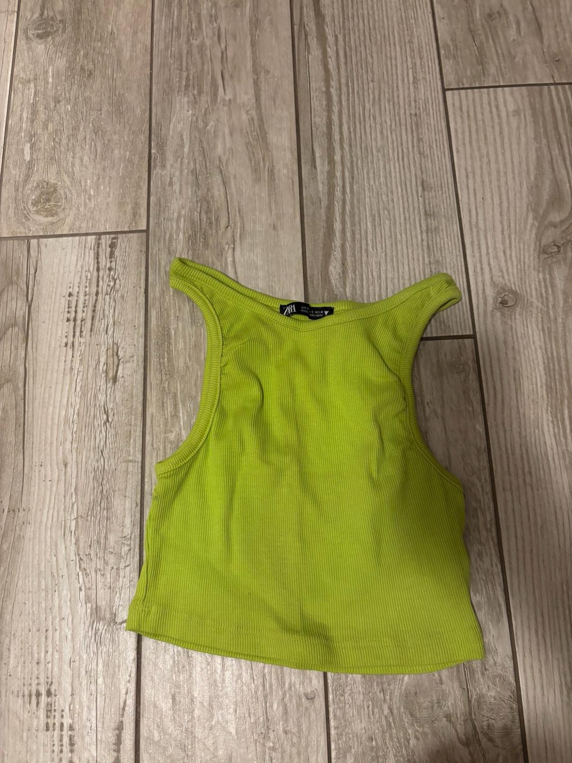 Sleeveless neon green ribbed knit crop top on a wooden floor. The ZARA label is visible.