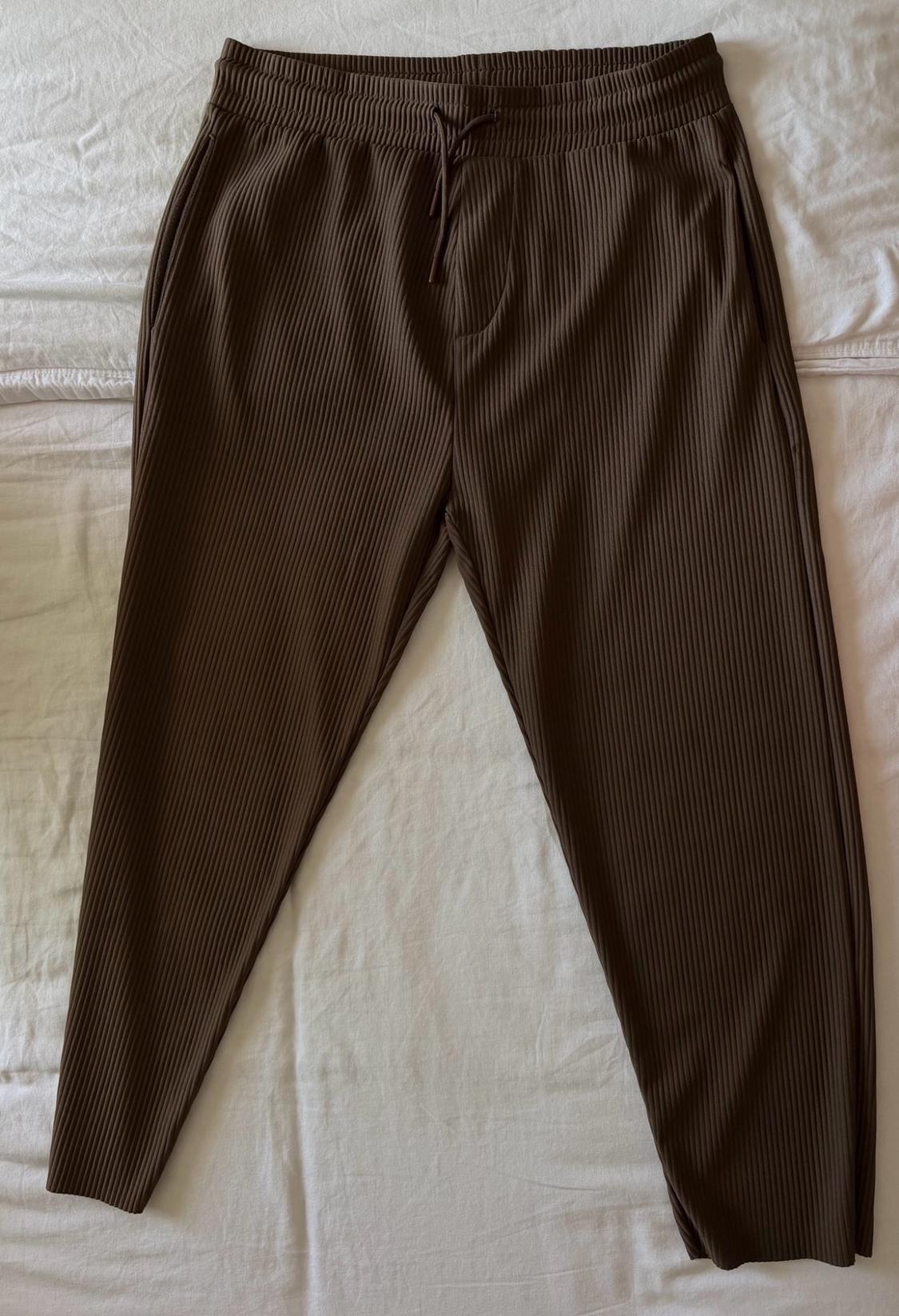 Brown ribbed trousers with an elasticated drawstring waist, laid out on relaxed-style crumpled white fabric.