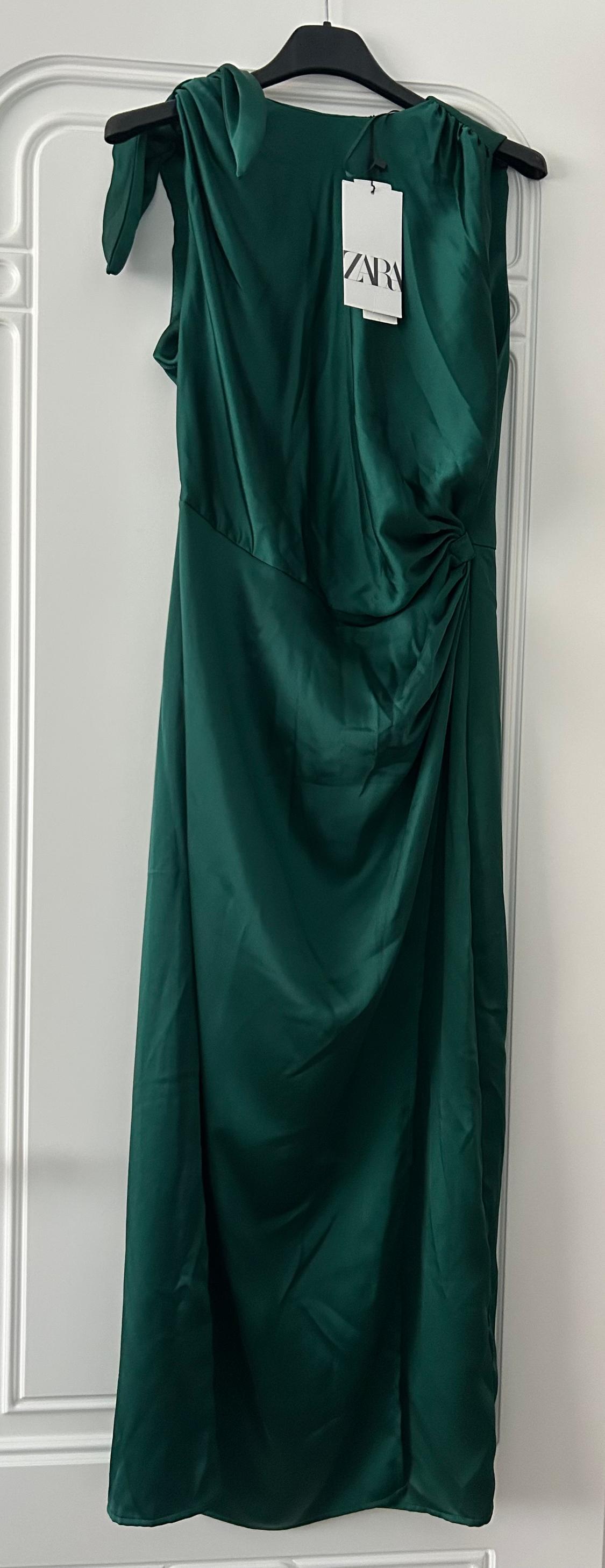 Emerald green maxi dress hanging on a black hanger, with a visible label that reads "ZARA", against a white background.