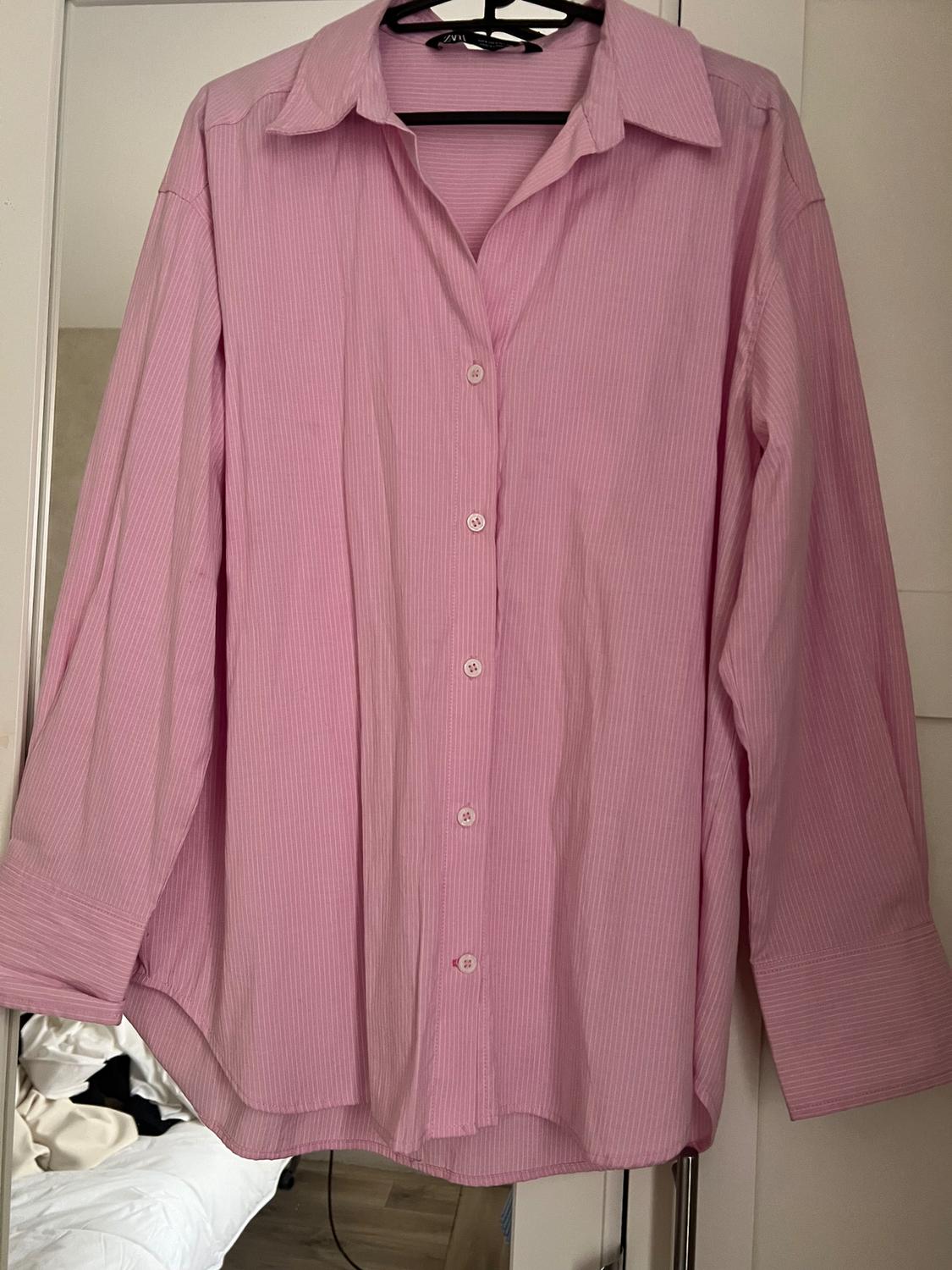 Light pink striped shirt hanging on a black hanger. White wardrobe background and messy bed.