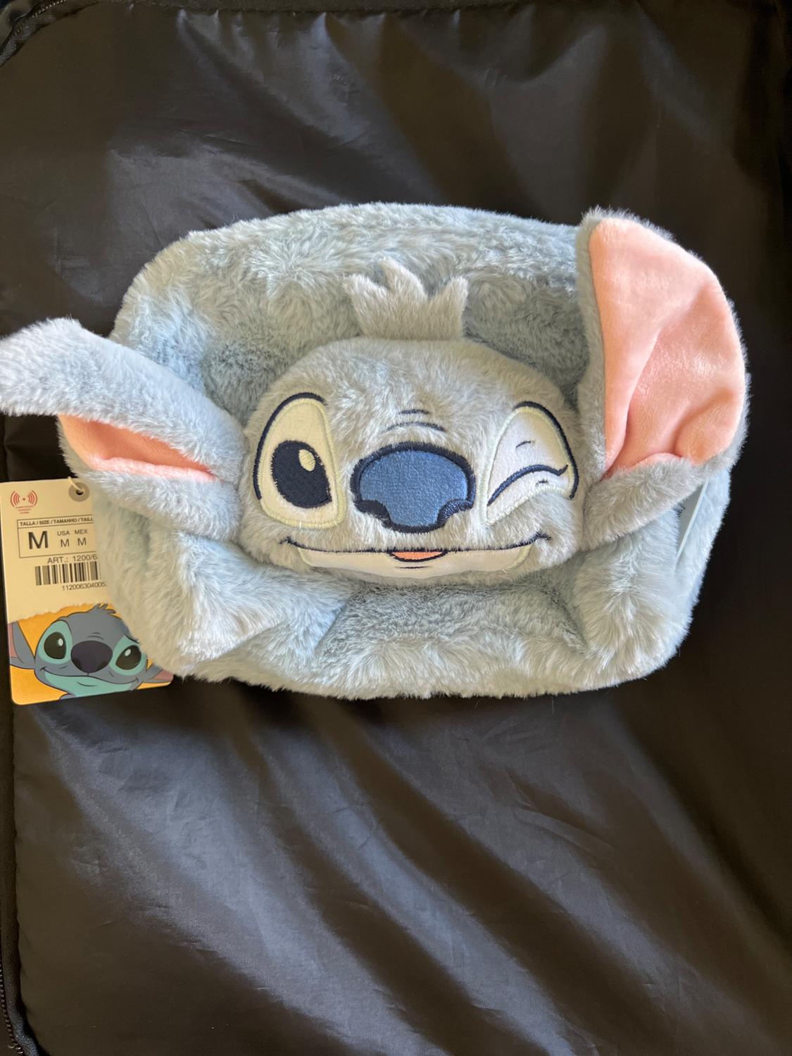 Blue plush beanie with a winking animated character design, large pink ears, and a size M label on a black background.