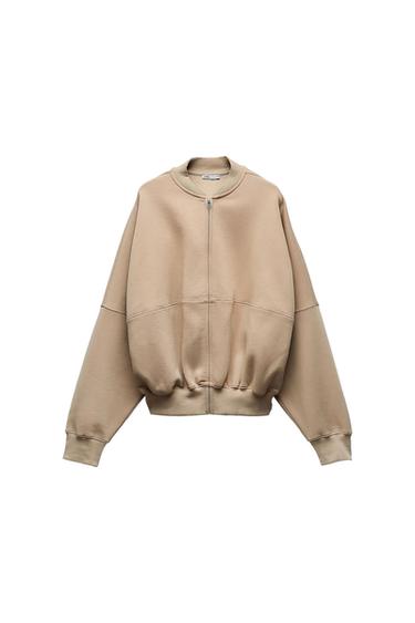 Beige sweatshirt with front zip, ribbed collar and cuffs. Features dropped shoulders and horizontal seam detail on a white background.